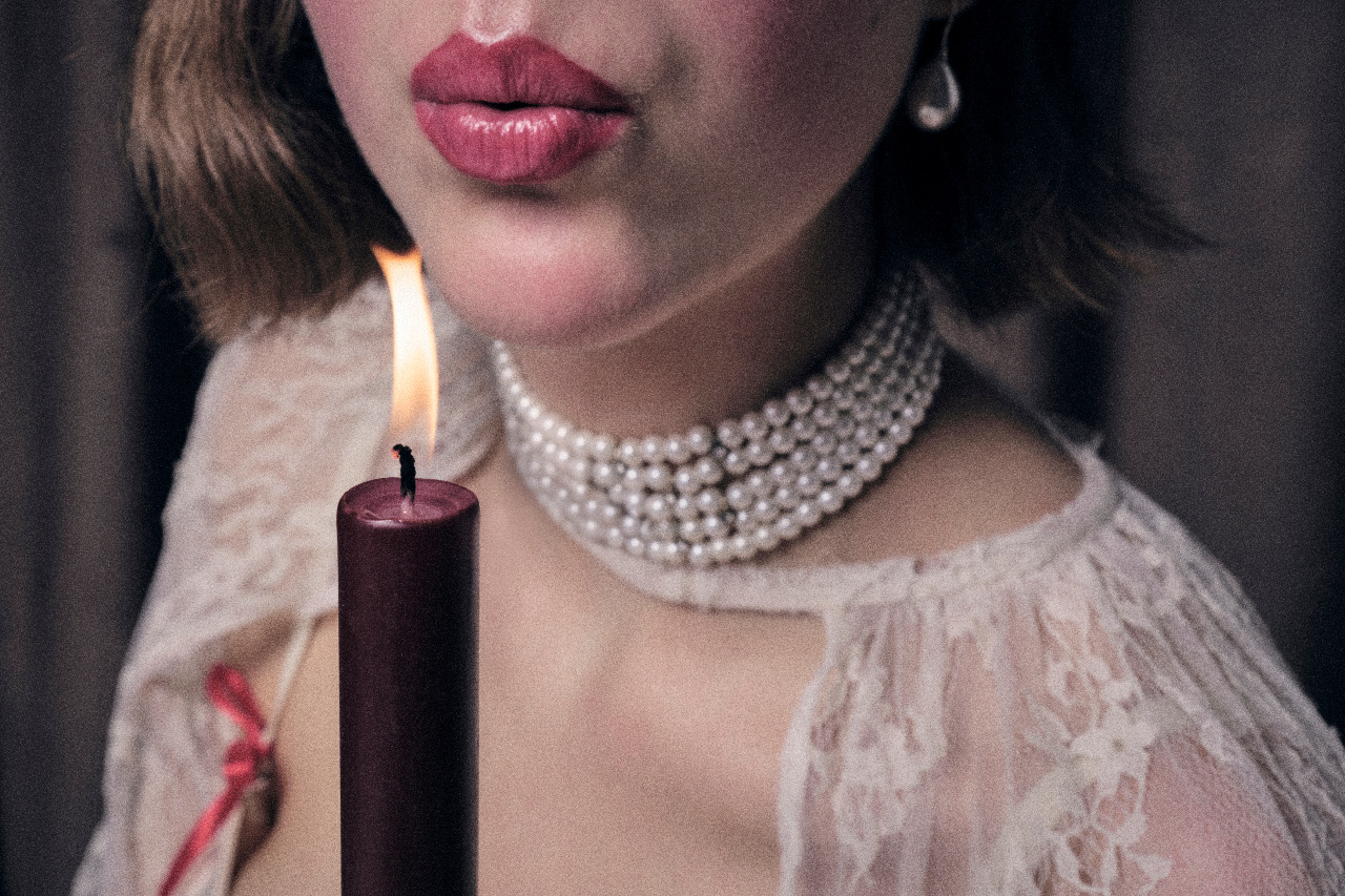A woman in pearls and lace blows out a dark candle