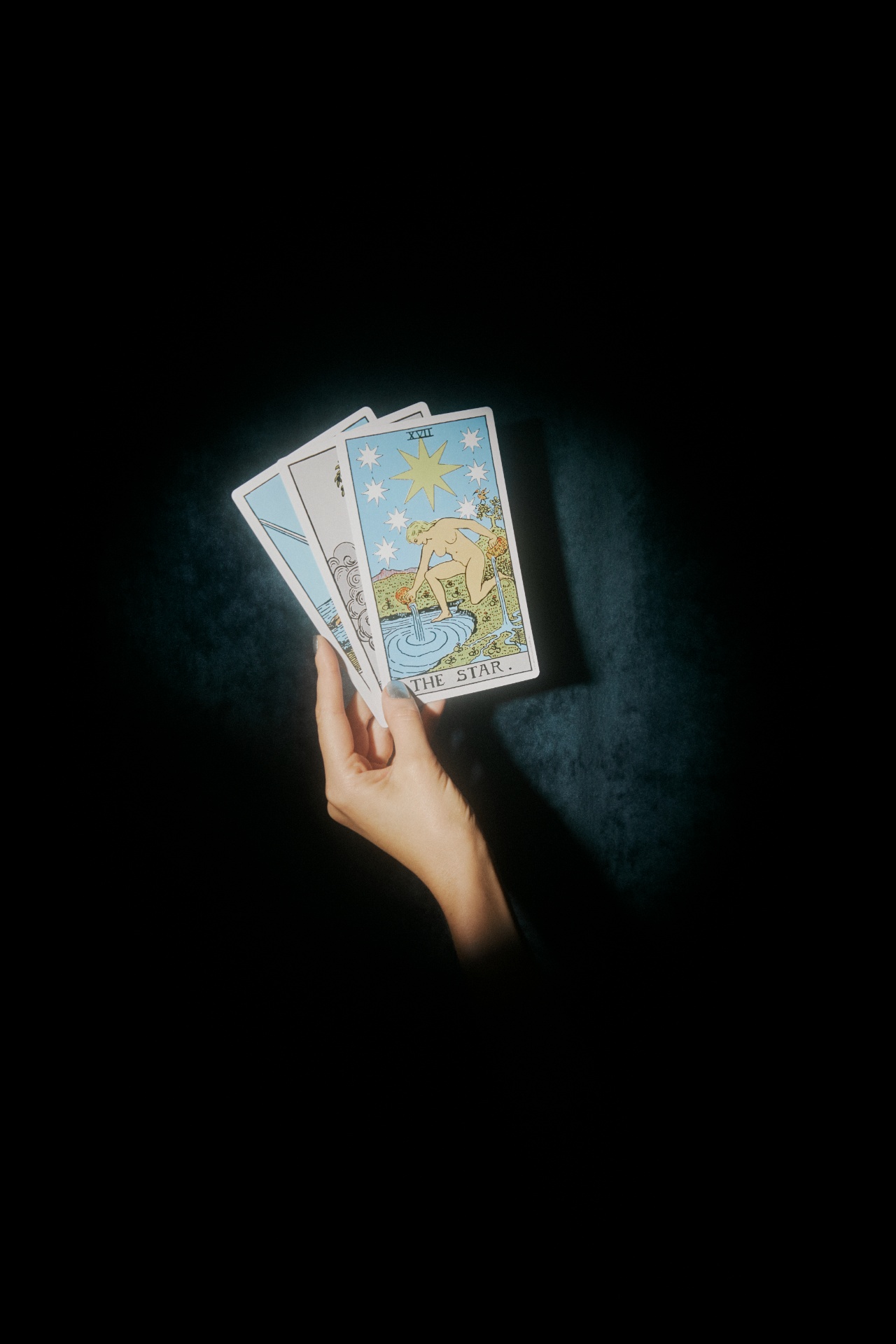 A hand fanning tarot cards in a spotlight — reading incomplete information